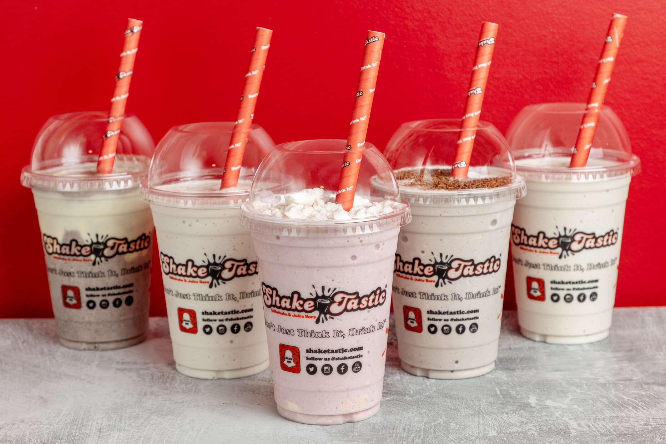 A lineup of ShakeTastic milkshakes topped with cream, chocolate and biscuit against a bold red backdrop